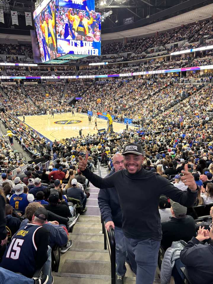 Okey on the stairs at a Denver Nuggets game, arena packed behind him