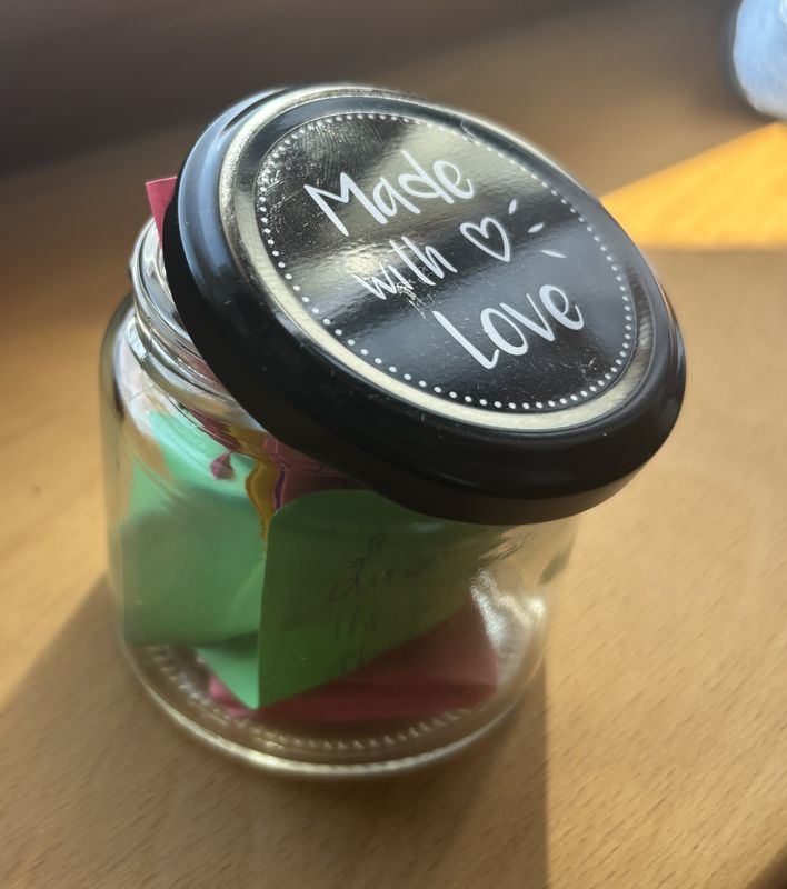 A small glass jar of folded coloured notes, its lid handwritten with the words Made with Love